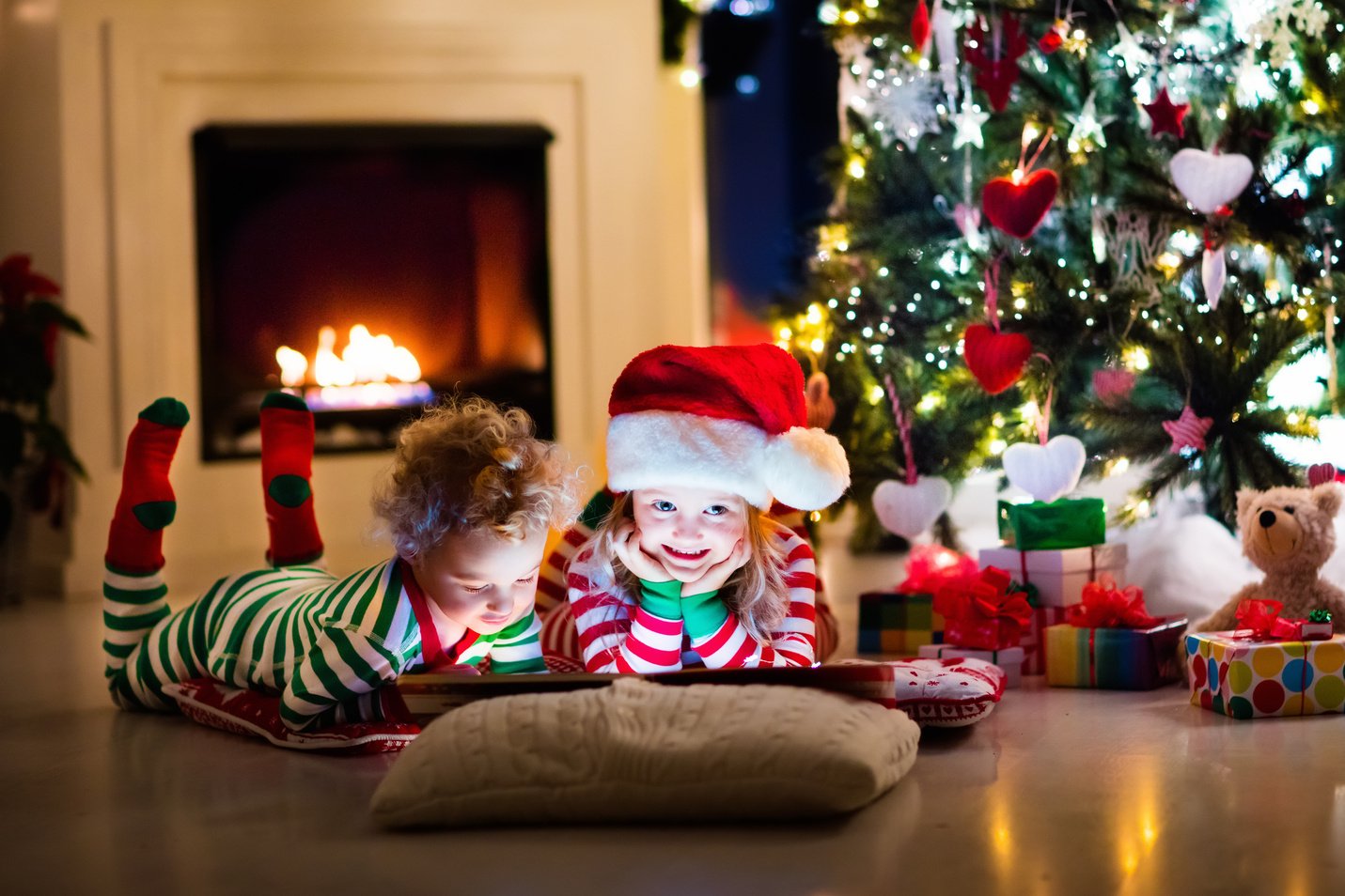 Kids in pajamas reading book under Christmas tree